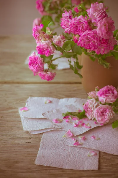 Roze rozen met papieren op houten tafel — Stockfoto