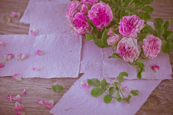 Pink roses with papers on wooden table — Stock Photo, Image