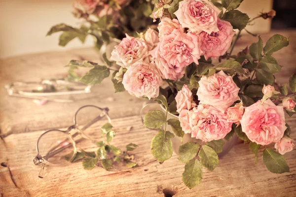Ahşap masa gözlüklerle pembe güller — Stok fotoğraf