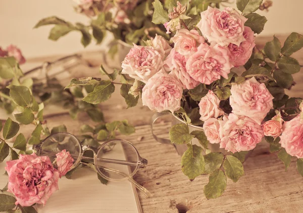 Pink roses with glasses on wooden table — Stock Photo, Image