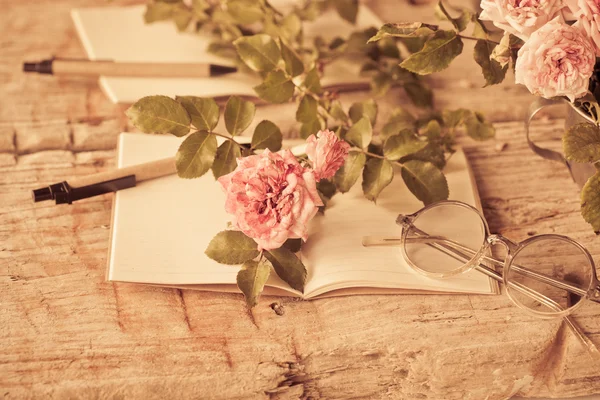 Pink roses with glasses on wooden table — Stock Photo, Image