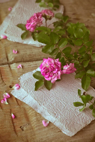 Roze rozen met papieren op houten tafel — Stockfoto