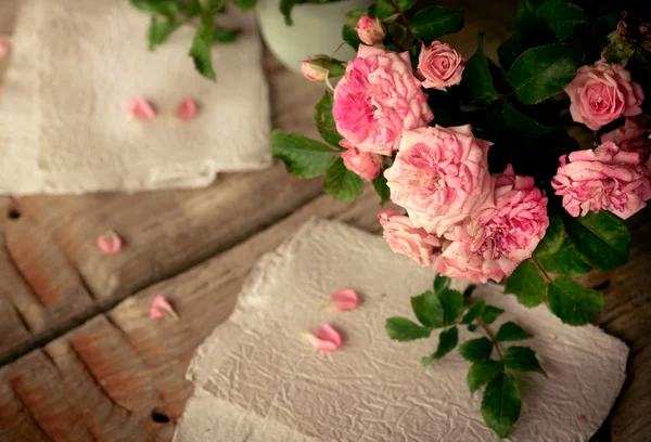 Pink roses with papers on wooden table — Stock Photo, Image