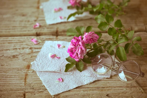 Roze rozen met bril op houten tafel — Stockfoto