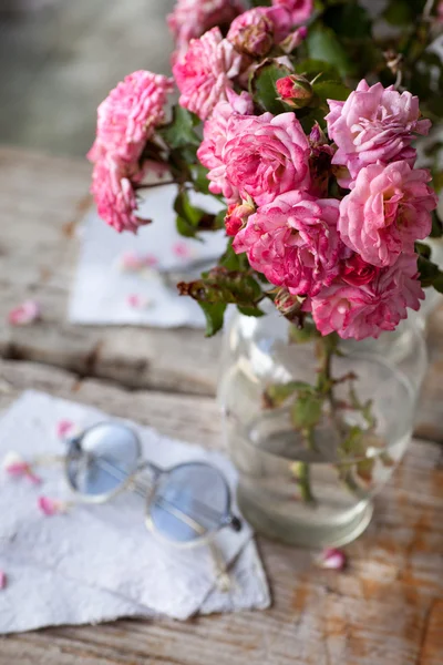 Pink roses with glasses on wooden table — Stock Photo, Image