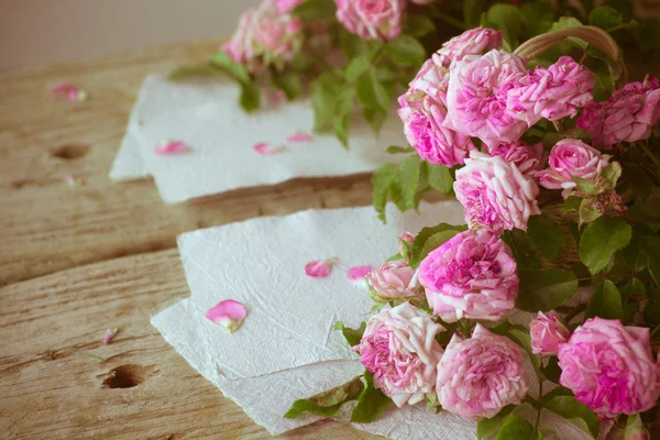 Rosa rosor med papper på träbord — Stockfoto