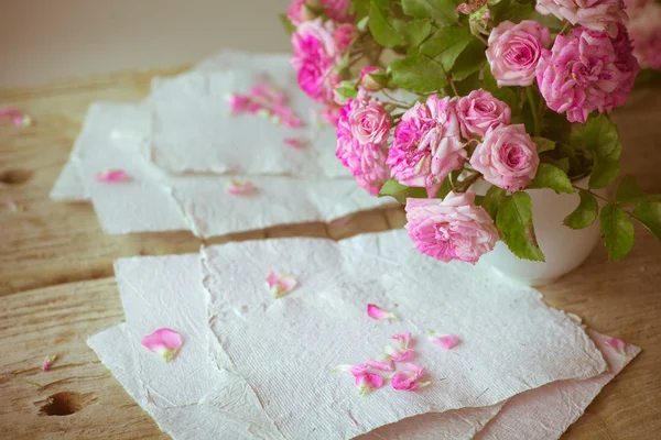 Pink roses with papers on wooden table — Stock Photo, Image