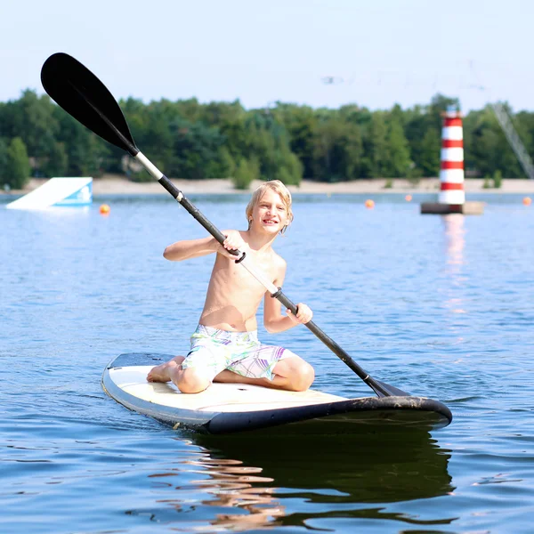 Adolescente acampando y disfrutando de pie remo en el lago — Foto de Stock