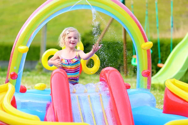 Menina pequena feliz espirrando na piscina inflável no jardim — Fotografia de Stock