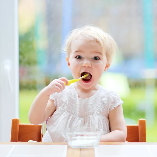 Маленькая девочка ест йогурт из ложки — стоковое фото