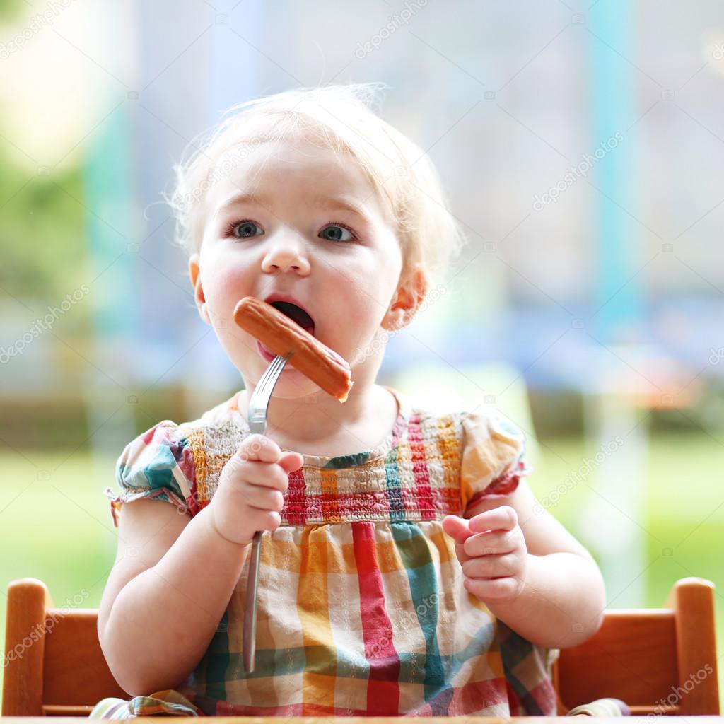 Funny little girl eating sausage from fork
