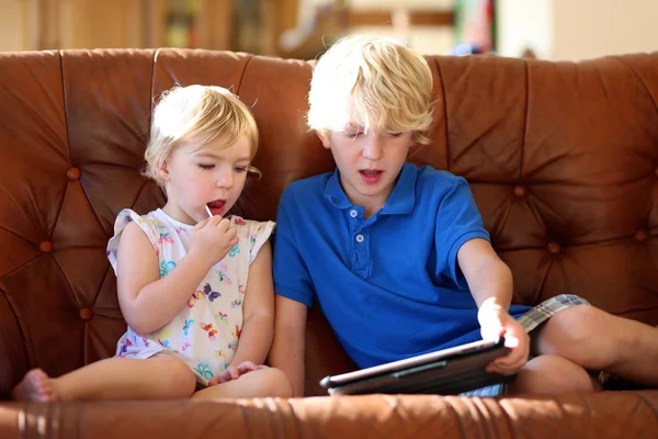 Irmão e irmã brincando com tablet pc no sofá — Fotografia de Stock