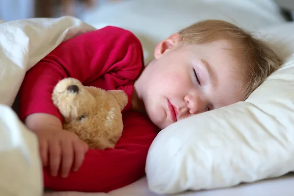 Oyuncak ayı ile yatakta uyuyan bebek kız — Stok fotoğraf