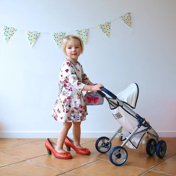 Cute little girl playing with toy pram and doll — Stock Photo, Image