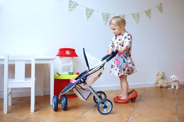 Niedliches kleines Mädchen spielt mit Spielzeug Kinderwagen und Puppe — Stockfoto