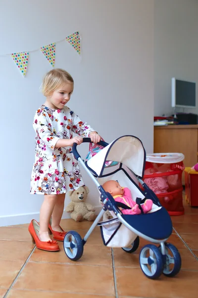Cute little girl playing with toy pram and doll