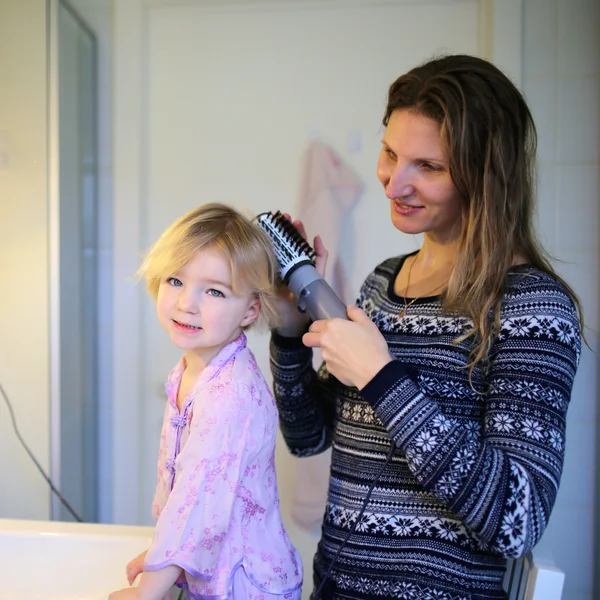 Madre e hija pequeña cepillando el cabello usando estilista — Foto de Stock