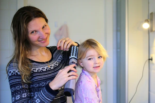 Matka a malá dcera kartáčování vlasů pomocí kulmy — Stock fotografie