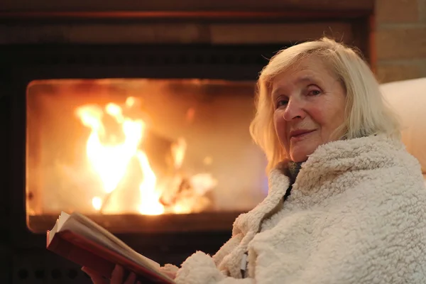 Senior lady relaxing at home by fireplace — Stock Photo, Image