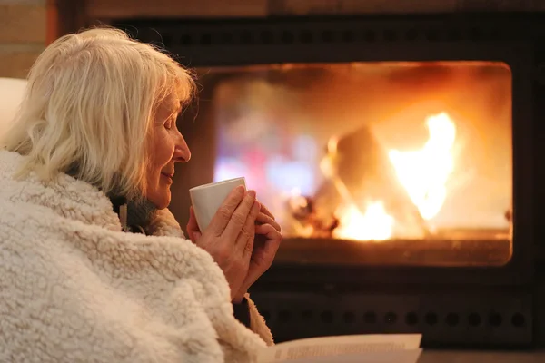 Seniorin entspannt zu Hause am Kamin — Stockfoto