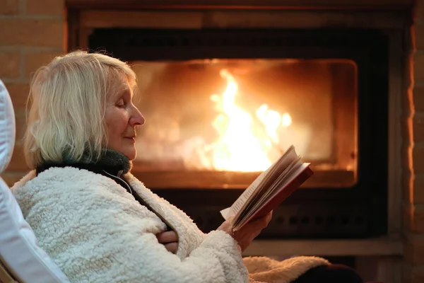 Senior dame ontspannen thuis bij open haard — Stockfoto