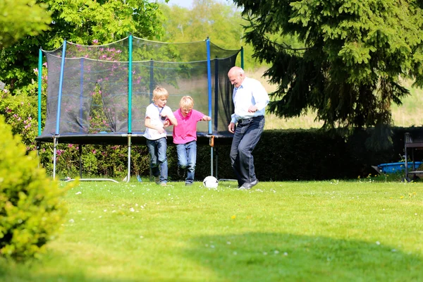 Дедушка с внуками играет в футбол в саду — стоковое фото