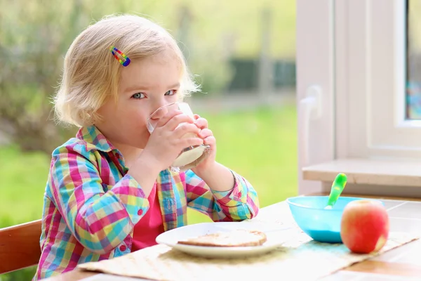 Liten flicka med rostat bröd och mjölk till frukost — Stockfoto