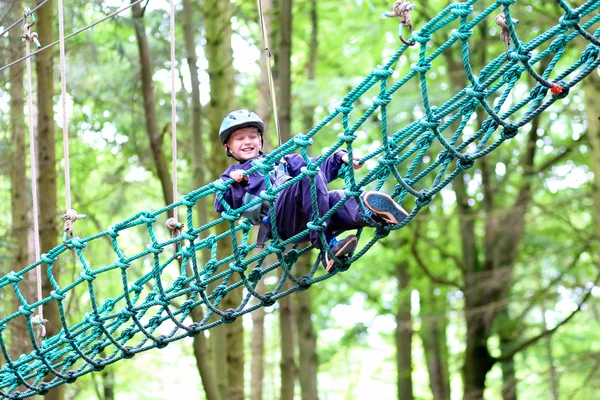 Happy school boy climbing in adventure park — Stock Photo, Image