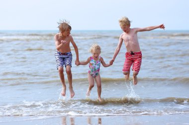 Kids having fun on the beach jumping over the waves