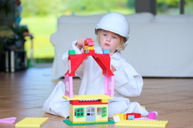 Toddler girl wearing safety helmet playing with building blocks