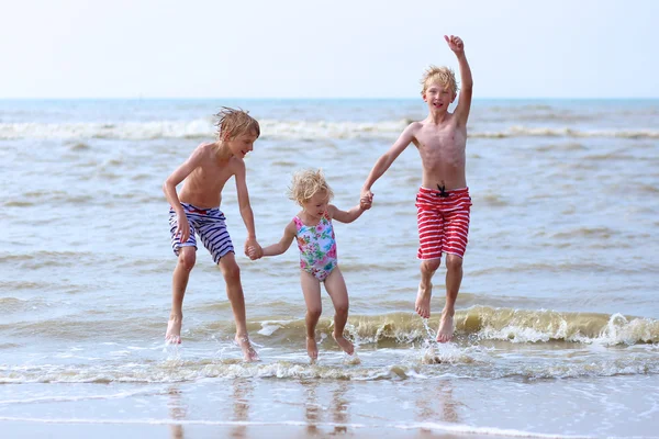 Niños divirtiéndose en la playa saltando sobre las olas — Foto de Stock