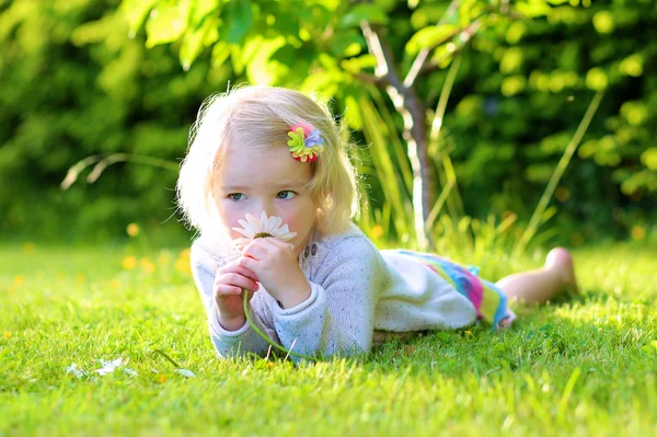 Маленький ребенок играет в саду лежа в траве — стоковое фото