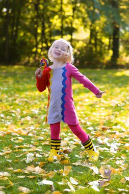 Happy girl with lollipop having fun in autumn park