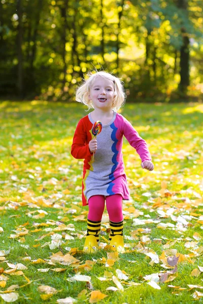Chica feliz con piruleta divertirse en el parque de otoño —  Fotos de Stock