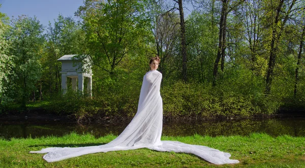 Mujer en un vestido con un tren y un estanque forestal — Foto de Stock