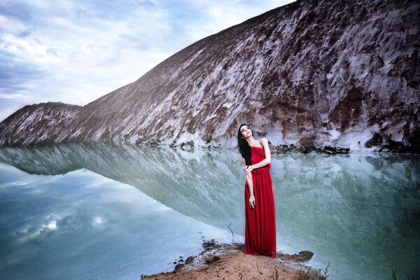 A girl in a red dress is posing near the river bank