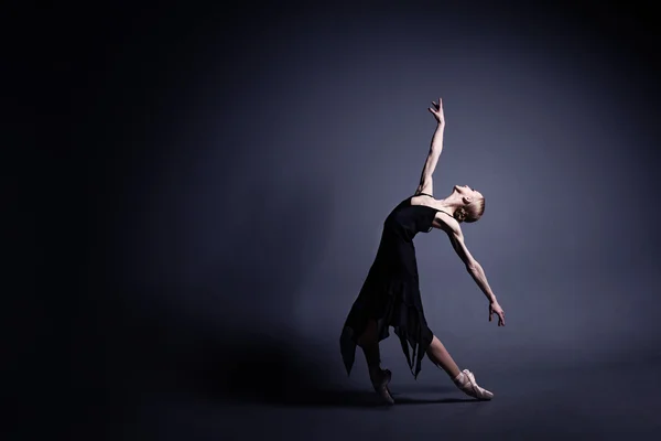 Mladá baletka v tmavé látky tancuje v temnu fotostudia — Stock fotografie