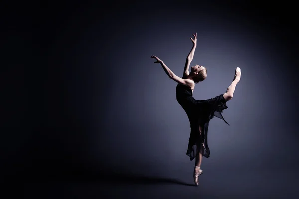 Junge Ballerina in dunklem Tuch tanzt im Dunkeln des Fotostudios — Stockfoto