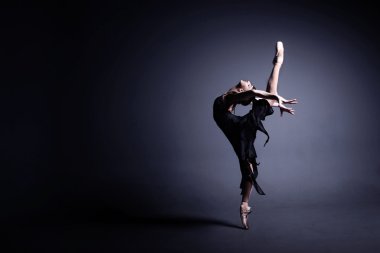 Young ballerina in dark cloth is dancing in a dark of the photostudio clipart