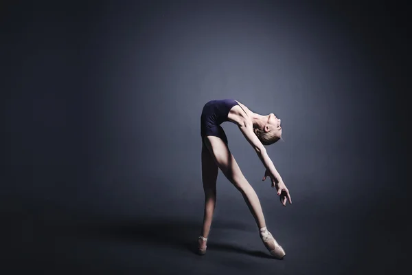Молодая балерина в темной одежде танцует в темноте фотостудии — стоковое фото