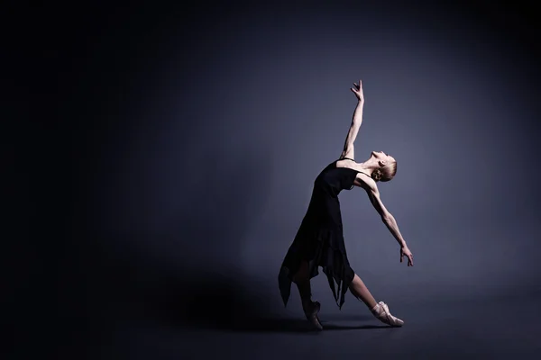 Young ballerina in dark cloth is dancing in a dark of the photostudio — Stock Photo, Image