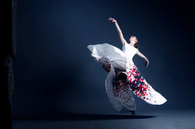 Young ballerina with a perfect body is dancing in the photostudio in different dresses