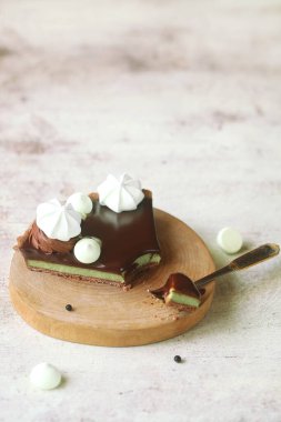 Çağdaş Çikolata Matcha Çayı Turtası Çikolata Ayna Cilalı Meringue Kurabiyeleri ve Çikolata Elementleri ile süslenmiş açık bej arka planda, tahta bir tahta üzerinde.