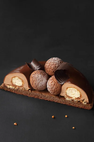 Contemporary Chocolate Mousse Cake with Craquelin Choux Pastry, covered with chocolate mirror glaze, on a dark background.