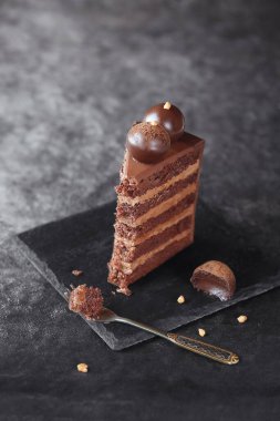 Slice of Contemporary Chocolate Truffle Layer Cake with chocolate smudge, decorated with handmade chocolate truffles, on a dark gray background.
