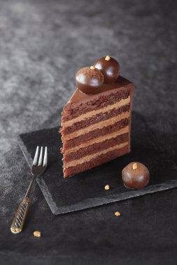 Slice of Contemporary Chocolate Truffle Layer Cake with chocolate smudge, decorated with handmade chocolate truffles, on a dark gray background.