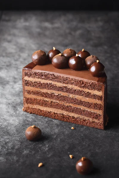 Contemporary Chocolate Truffle Layer Cake with chocolate smudge, decorated with handmade chocolate truffles, on a dark gray background.