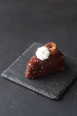 Çağdaş Üçgen Çikolatalı Vanilyalı Mousse Pastaları, doğranmış bademlerle kaplı, çikolatalı ganache ve kremalı kurabiyelerle süslenmiş, koyu gri bir arka planda..