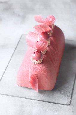 Çağdaş Ruby Chocolate, Red Currant ve Matcha Yule Log Mousse Pastası yakut çikolata kadife spreyiyle kaplanmış ve yakut çikolata elementleriyle süslenmiş gri bir arka planda..