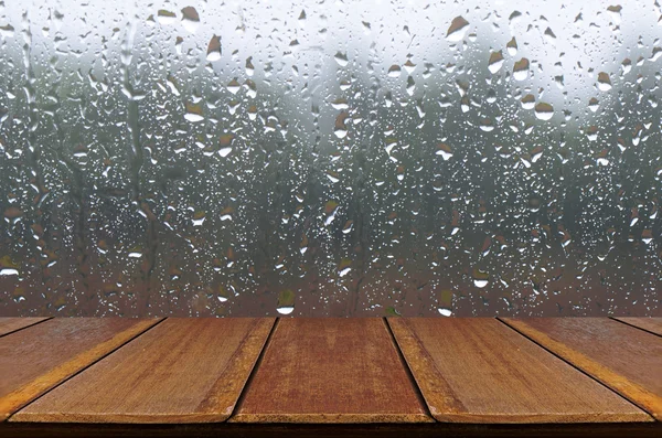 Gotas de chuva em fundo de janela de vidro com mesa de madeira . — Fotografia de Stock